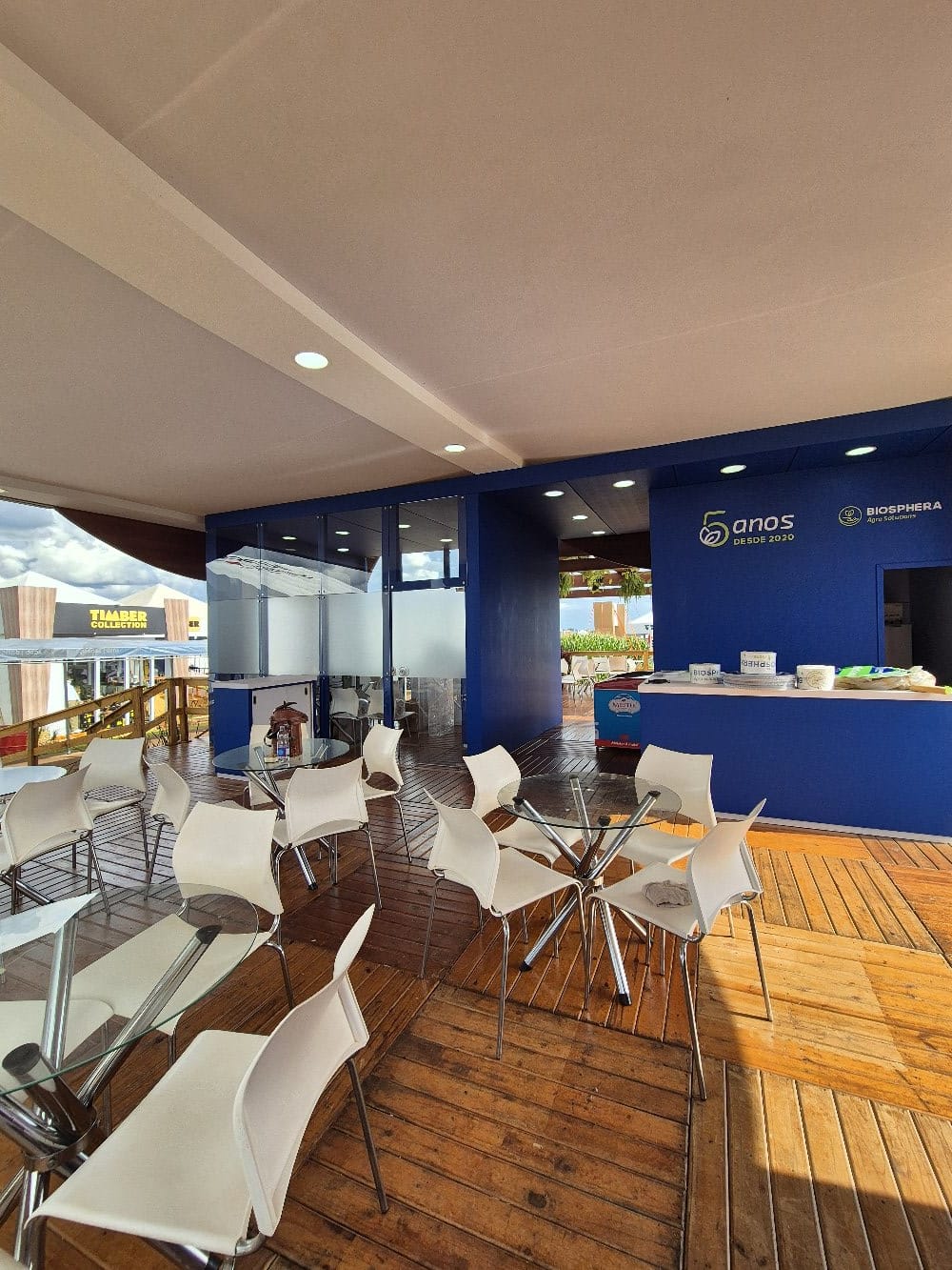 Lounge interno do stand Biosphera com mesas e painel 5 anos